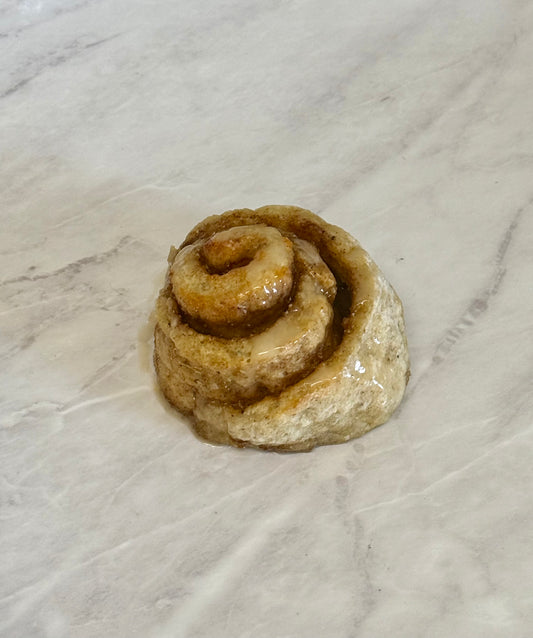 A single spiral-shaped pastry or bread roll with a glossy brown glaze, placed on a light marble-like surface.