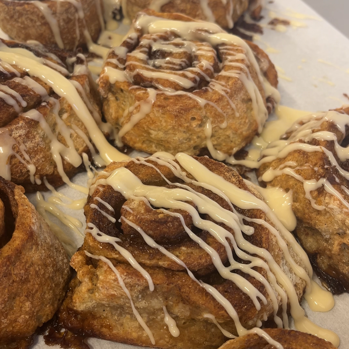 Close-up of several cinnamon rolls or sweet rolls on a baking sheet, topped with white icing drizzle.