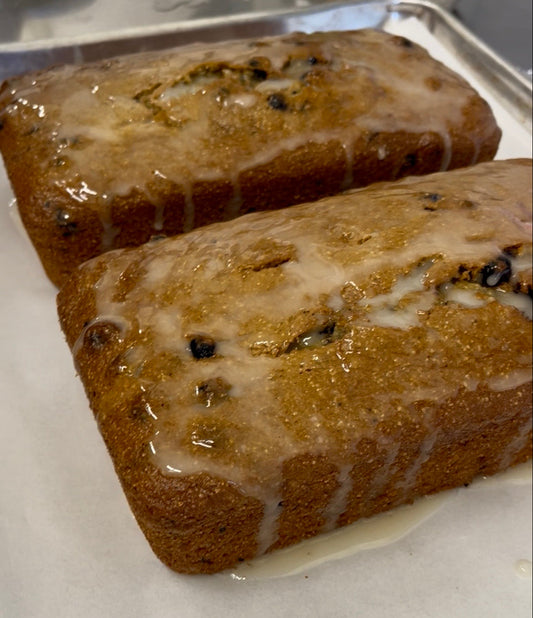 Two rectangular loaves of blueberry bread with white icing glaze, resting on a metal baking pan lined with parchment paper.